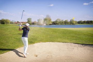 Golf player pitching from bunker.