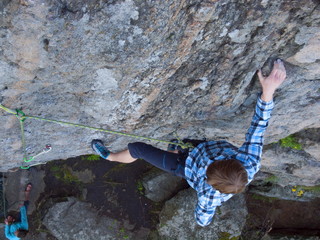 Handsome man in a plaid shirt climbs on the rock.