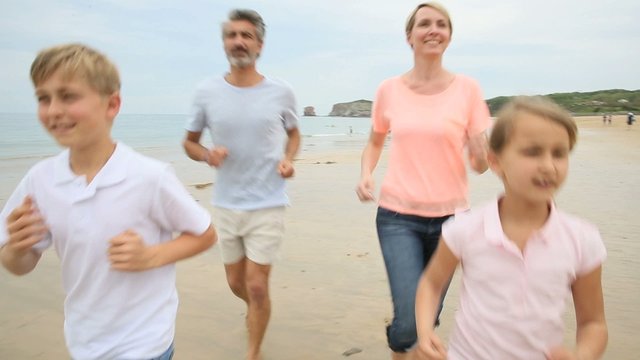 Happy family of four running on a sandy beach