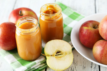 Jars of baby puree with apples on white wooden background