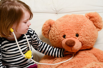 Cute, blonde girl playing doctor with plush toy bear 