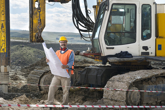 Mechanic engineer checking road plans in front of drilling pile