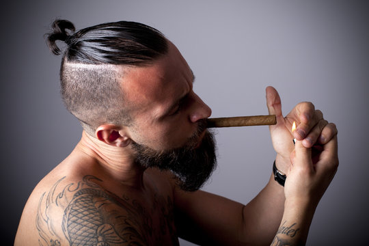 Joven hipster con tatuajes encendi&eacute;ndose un puro