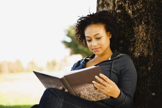 African woman holding book under tree