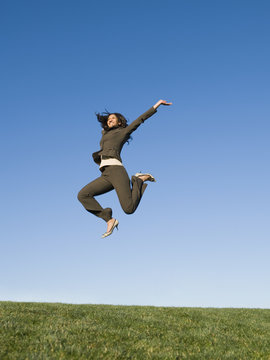 Mixed race businesswoman jumping in field