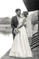 Fototapeta premium Black and white shot of bride and groom posing on pier at river