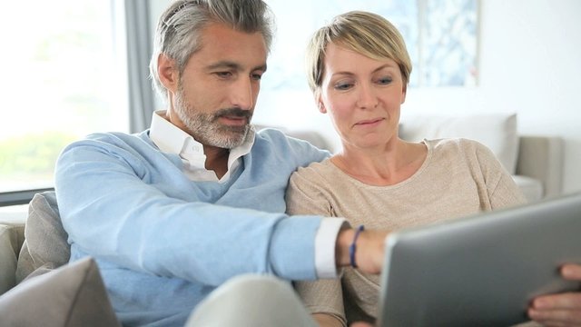 Middle-aged couple websurfing on internet with touchpad