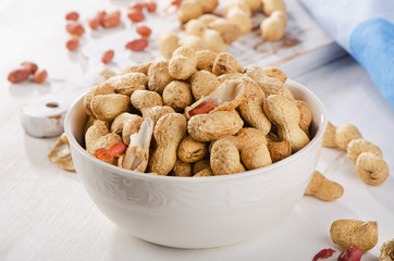 Peanuts in shells in  white bowl.