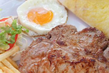 Grilled steaks, French fries, fried egg and vegetables
