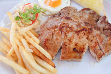 Grilled steaks, French fries, fried egg and vegetables