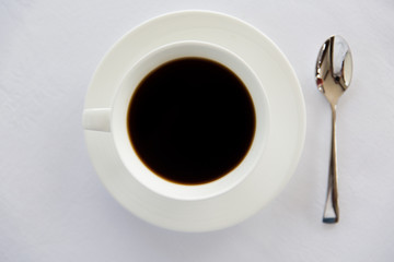 cup of black coffee with spoon and saucer on table