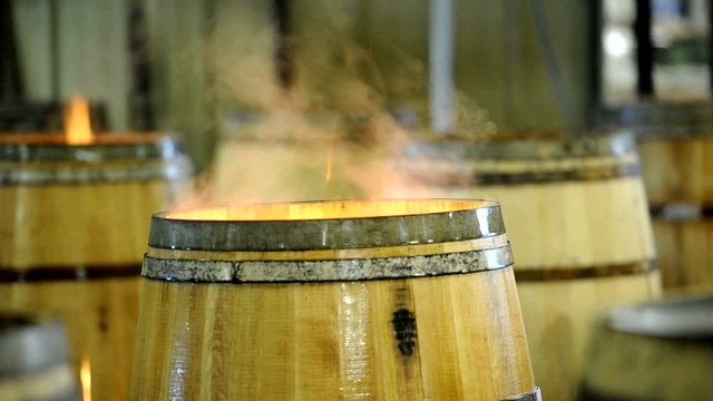 Flames rising from wood barrel and man stir the blaze.