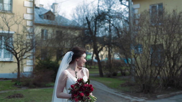 Young happy bride smiling holding bouquet of red flowers
