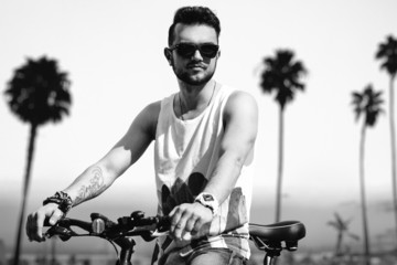Young hipster man on the beach in sunny summer day with bike
