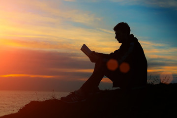 Silhouette of a man sitting on breakwater in evening near sea, r