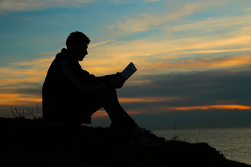 Silhouette of a man sitting on breakwater in evening near sea