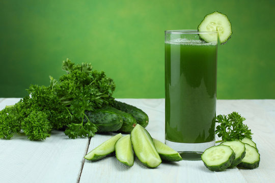 A glass of cucumber juice and fresh cucumber on a wooden table