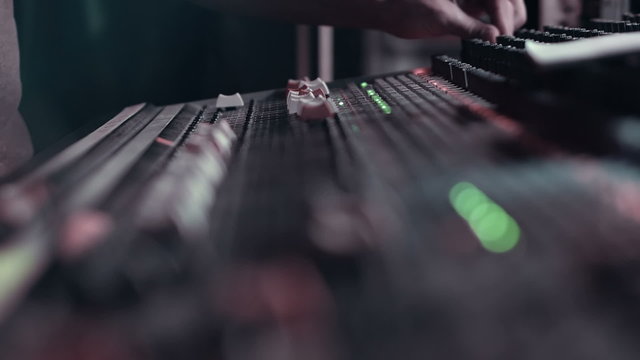 Audio Engineer adjusting faders on his mixing console desk