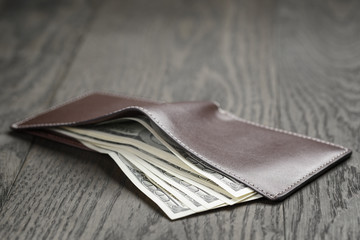 leather wallet on wood table with dollar bills