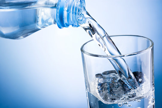 Close-up pouring water from bottle into glass on a blue backgrou