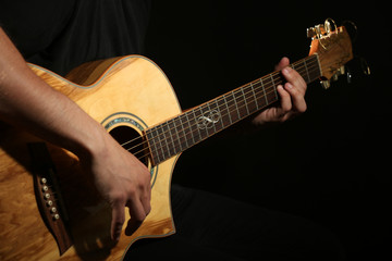 Fototapeta premium Young man playing on acoustic guitar on dark background