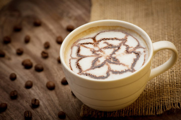 Cup of cappuccino served on wooden table with coffee beans in th