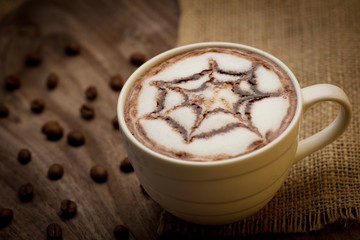 Cup of cappuccino served on wooden table with coffee beans in th