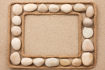 Beautiful frame with rope and white stones on sand