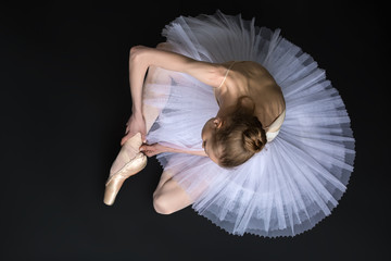 Young ballet dancer tying pointe sitting on the floor