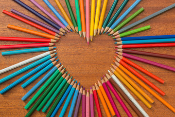 Colored pencils formed into a heart shape on a wooden table