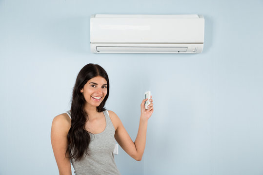 Woman With Remote Control In Front Of Air Conditioner