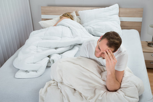 Depressed Man On Bed While Woman Sleeping