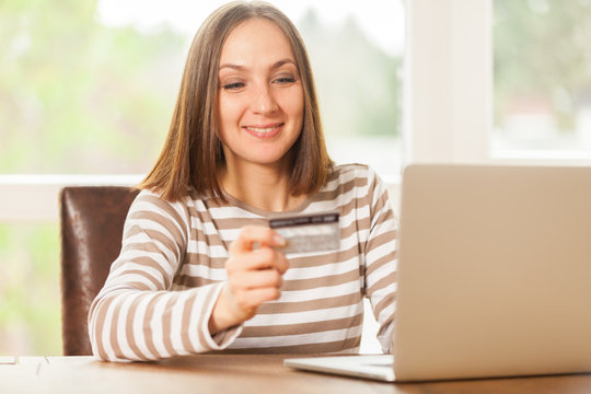 Young smiling woman holding a credit card in her hand while doin