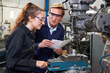 Engineer Showing Apprentice How to Use Drill In Factory