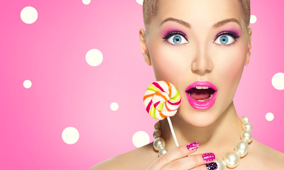 Funny girl eating lollipop over pink polka dots background