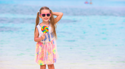 Adorable little girl have fun with lollipop on the beach
