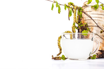 Isolated transparent cup of birch sap with birch leaves