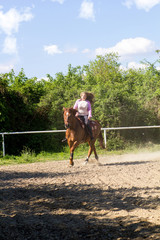young smiling girl riding her brown horse in a training field
