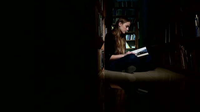 student girl sitting on floor and examines book in library