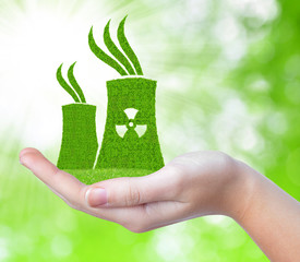 Nuclear power plant icon in hand on green natural background.