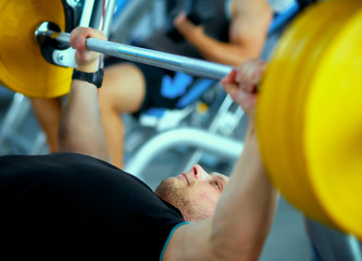 Fototapeta premium Young man lifting the barbell in gym with instructor
