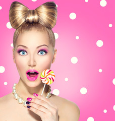 Funny girl eating lollipop over pink polka dots background