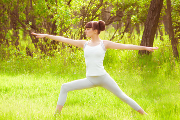 Young girl doing yoga on a green grass in summer