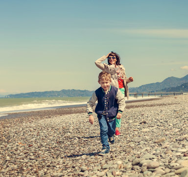 Little son with mother runs together at the sea coast