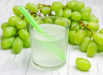 Glass of white grapes juice and grapes on background