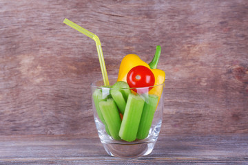 Sticks of celery with sweet pepper and cherry tomato in glass with tube on rustic wooden background