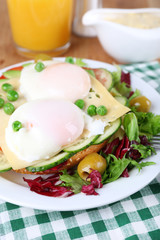 Sandwich with poached eggs, cheese and vegetables on plate on table close up