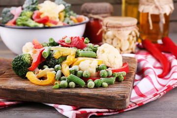Frozen vegetables on cutting board, on napkin, on wooden table background
