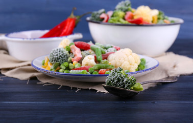 Frozen vegetables on plate on napkin, on wooden table background