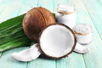 Fresh coconut oil in glassware and green leaf on color wooden table background